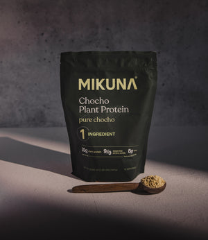 Mikuna Pure Chocho Plant Protein package with a wooden scoop of protein powder on a dark background
