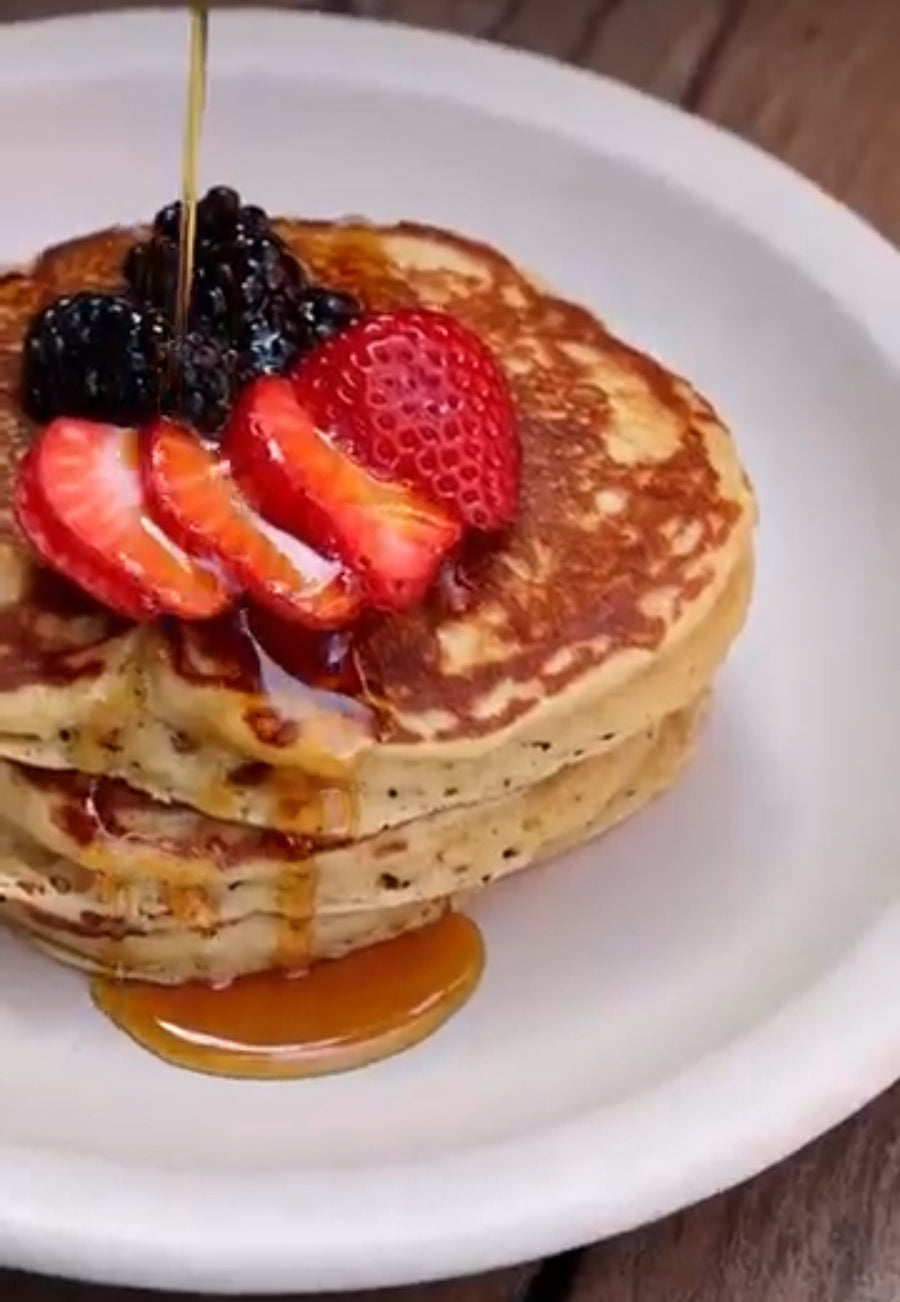 A stack of Erewhon chocho protein pancakes with berries and maple syrup