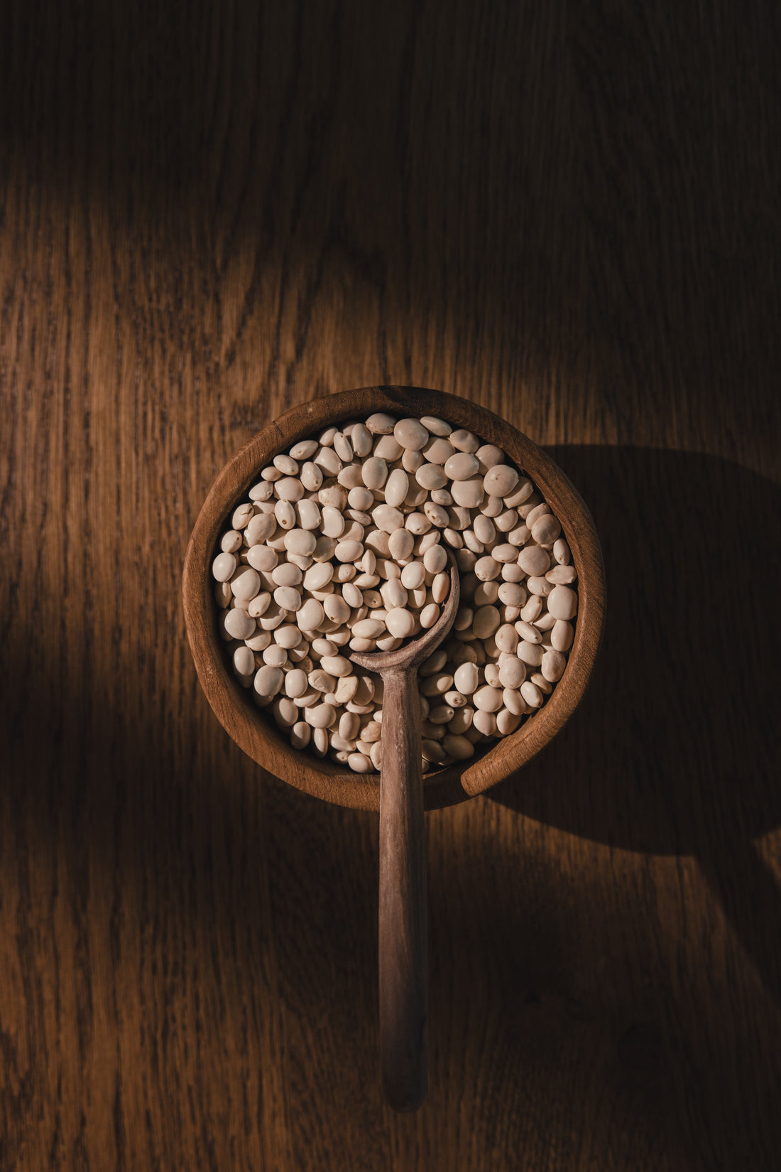 Hands holding a MIKUNA Chocho Plant Protein bag with a wooden scoop of powder above it