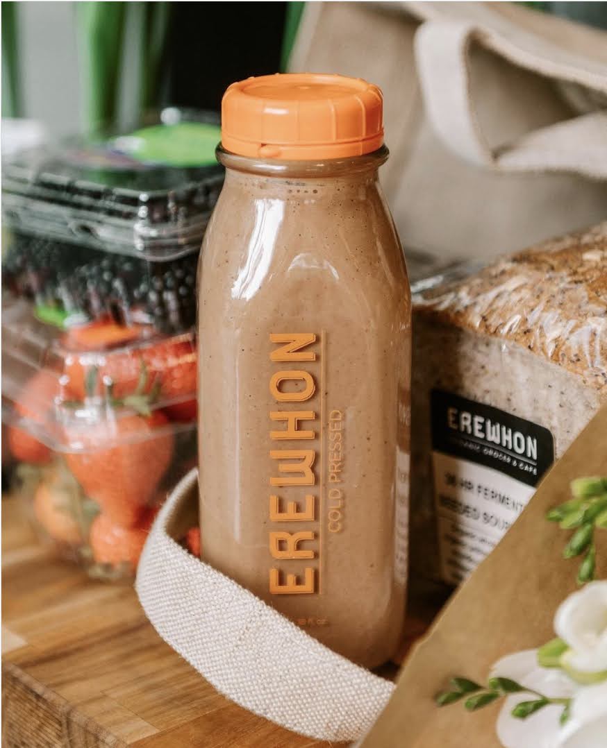 A Regenerada cold-pressed bottle styled with produce and an Erewhon bag